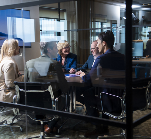 Five RGF Staffing employees discussing topics in a glass meeting room