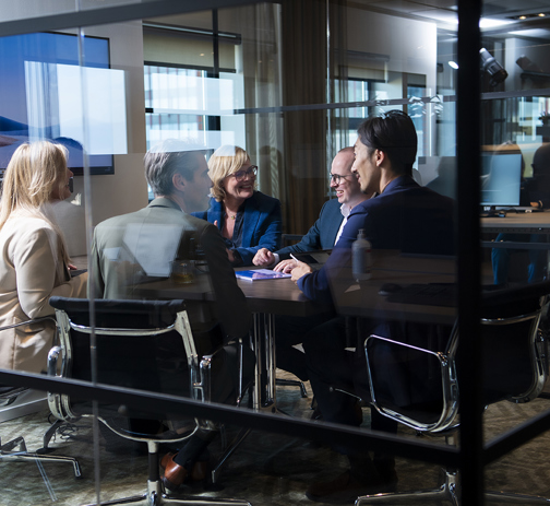 Five RGF Staffing employees discussing topics in a glass meeting room