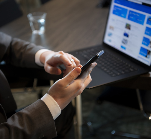 An office worker on his phone and a laptop on a desk in front of him