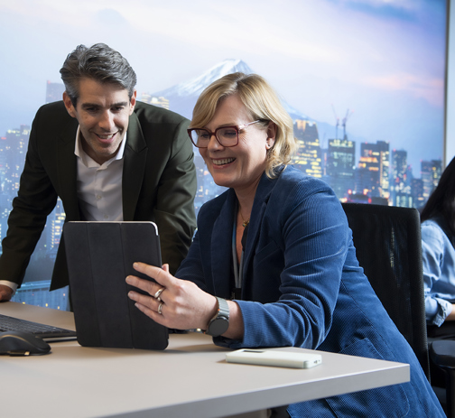 Two colleagues looking at a tablet screen from a desk in an office