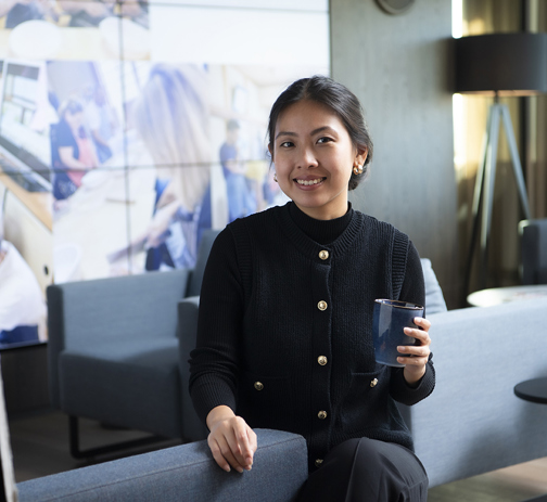 A RGF Staffing employee sitting on a lounge chair smiles into the camera, holding a cup
