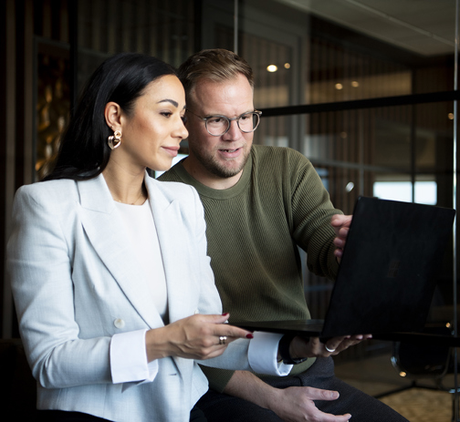 A picture of two colleagues looking at a laptop screen in the office